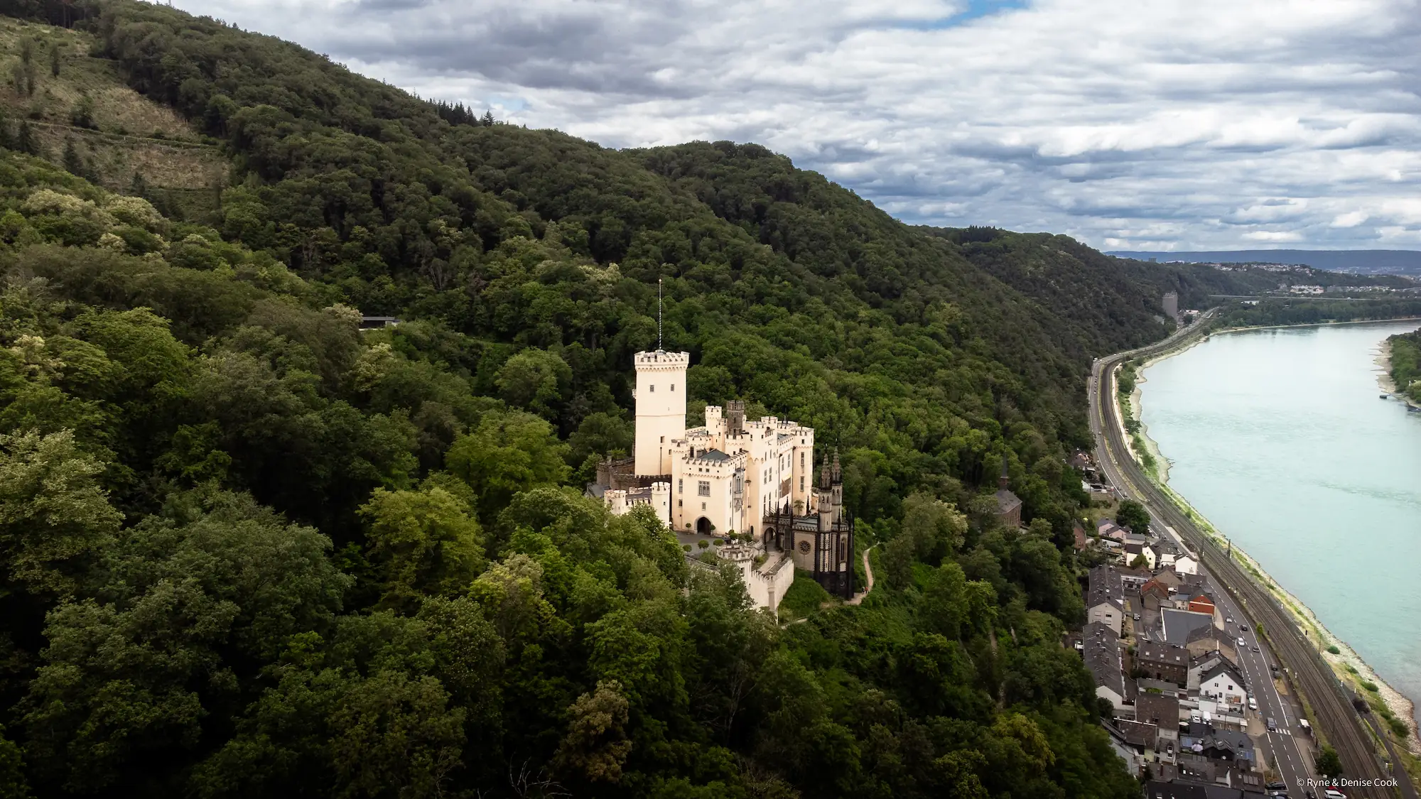 Aerial photo of Stolzenfels castle with a lush forest behind it and the Rhine river in view.