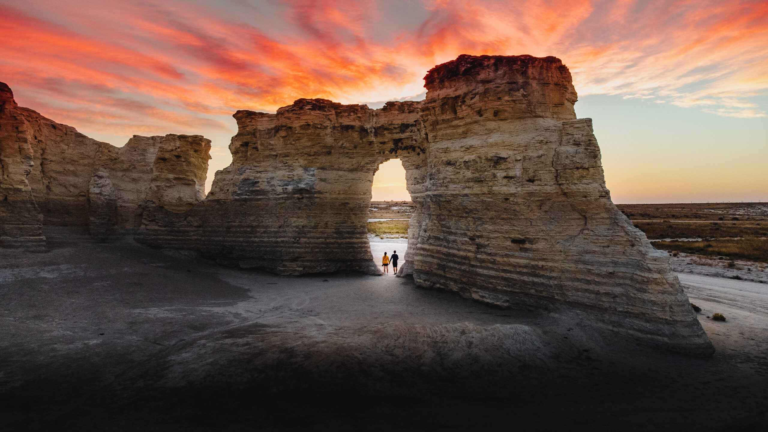 Young couple standing in an opening of a unique rock formation beneath a beautiful sunrise