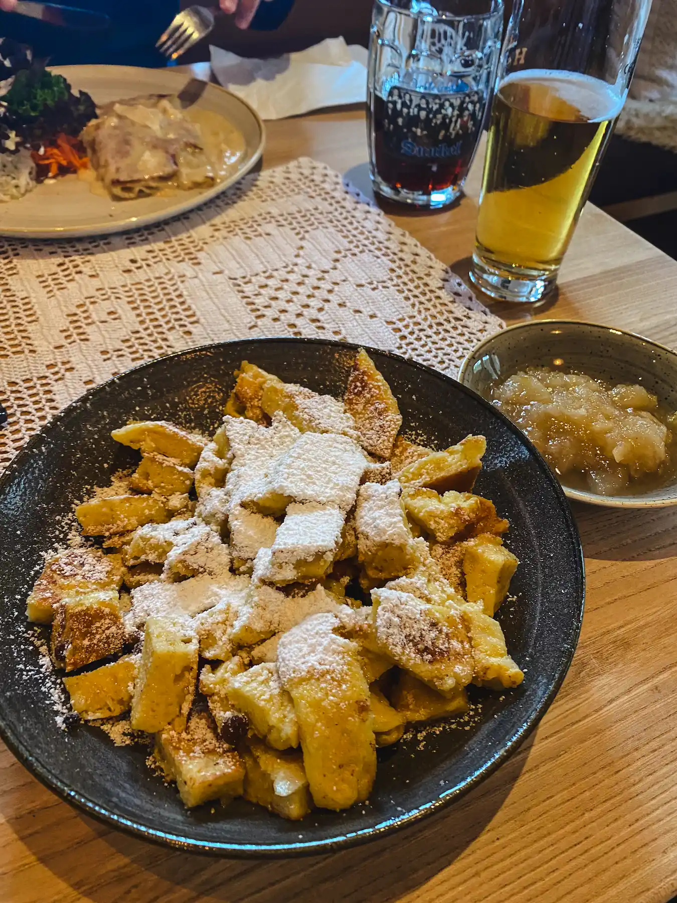 Kaiserschmarrn with powdered sugar and applesauce on table next to beers